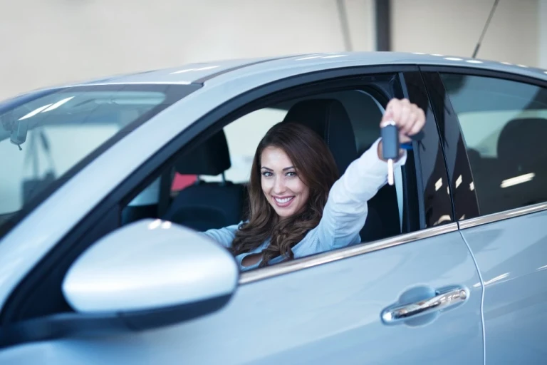 Femeie la volanul unei mașini, ținând cheia autoturismului în mână, imagine ilustrativă pentru închirieri auto cu FULL CASCO.